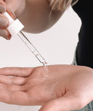 Droplets of  clear serum coming out of a dropper into a hand. 