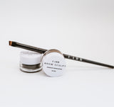 Black precision angle brush balanced on a jar of brow sculpt waterproof shaping pomade. A second brow sculpt eyebrow product is balanced on its side in front of the brush. 